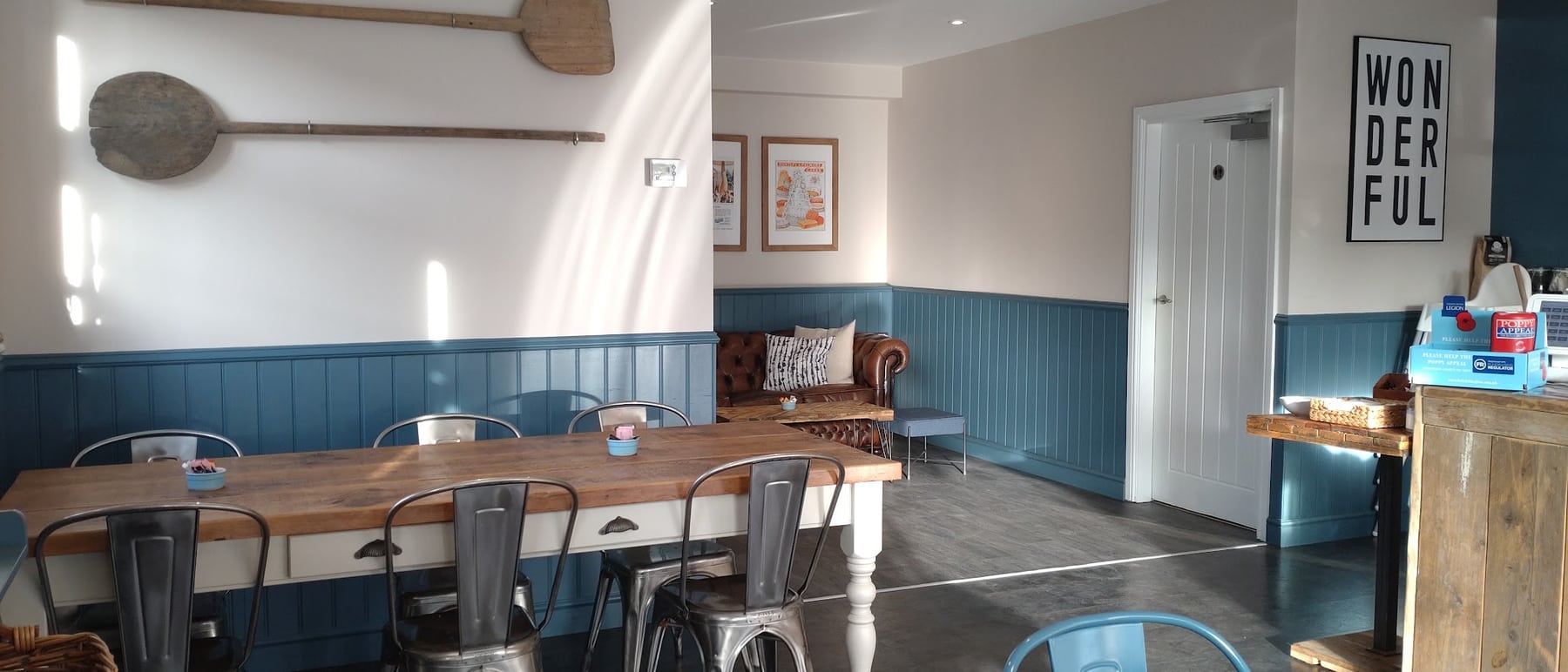 Sunlight across the long wooden table and blue panelling inside the café
